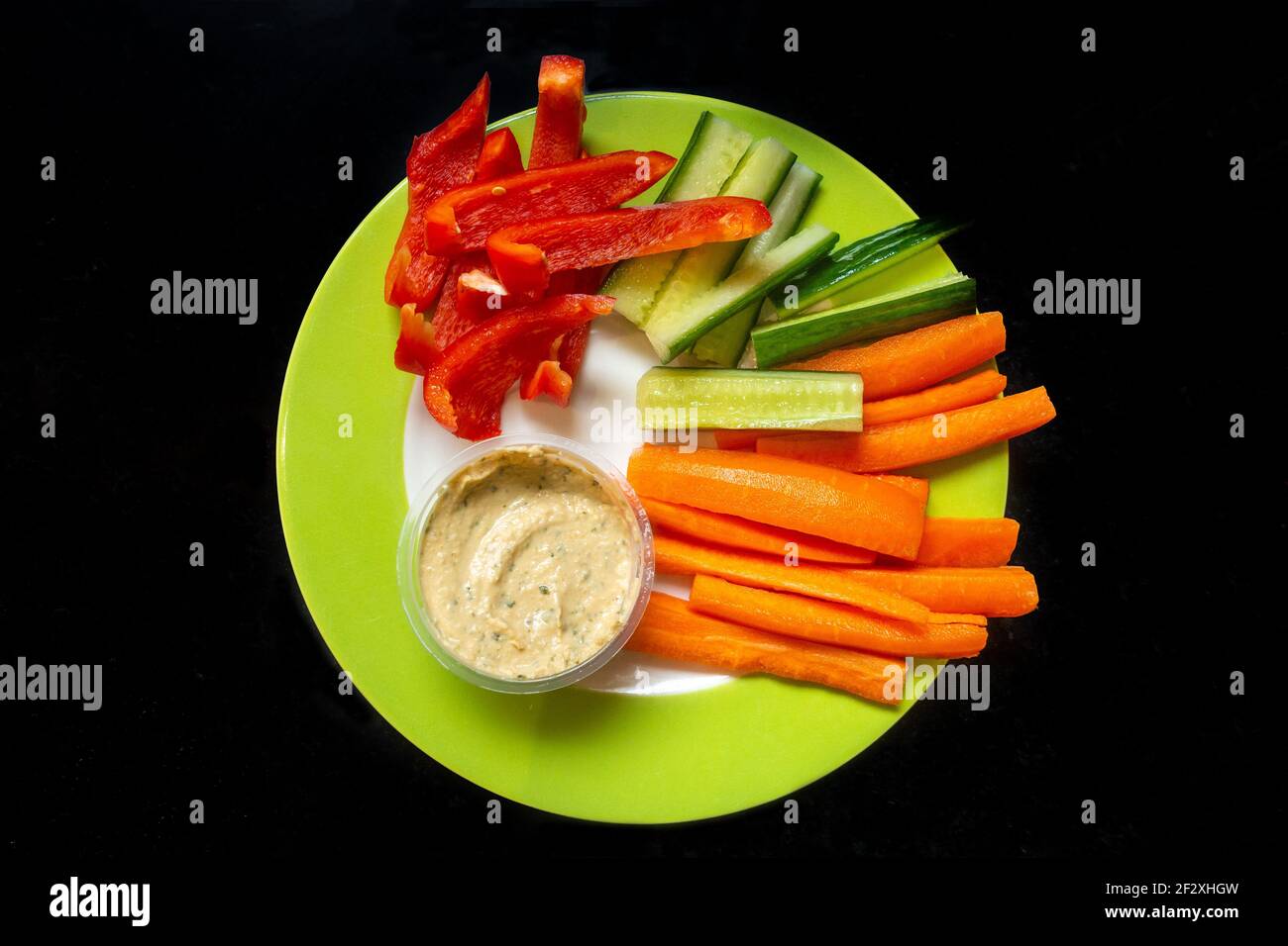 Healthy meal of sliced, raw vegetables with a humus dip isolated against a black background. Stock Photo
