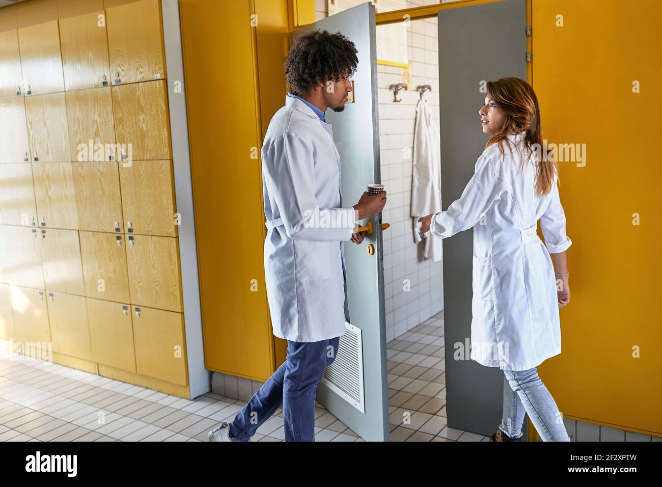 Two young interns entering dressing room together after shift Stock Photo