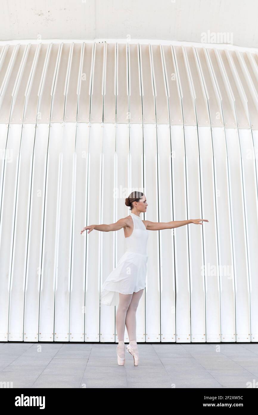 Young female ballet dancer in tiptoe in pointe shoes with raised leg and arm dancing on tiled pavement outdoors Stock Photo