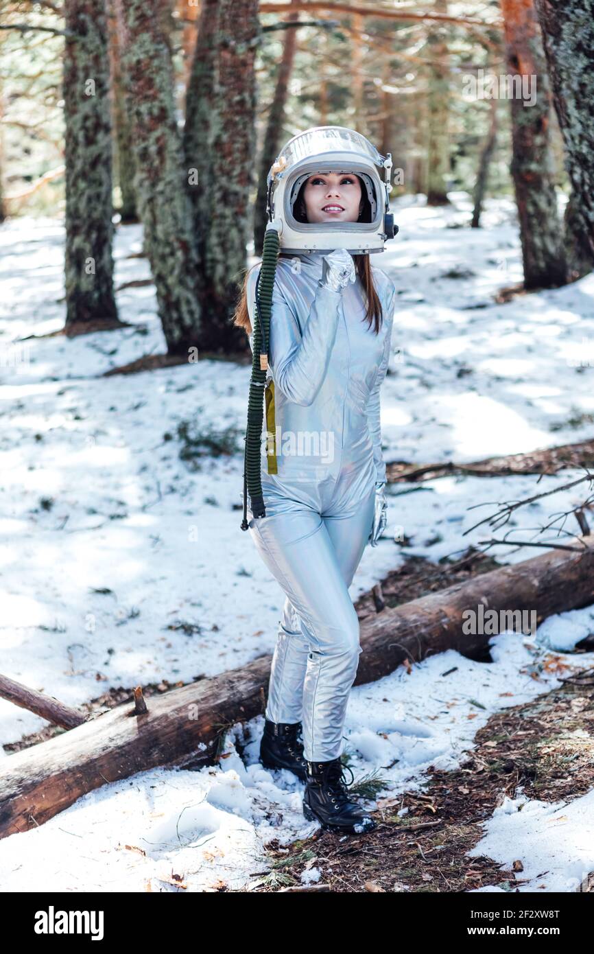 Focused young female astronaut in spacesuit and helmet looking away and standing in snowy woodland Stock Photo