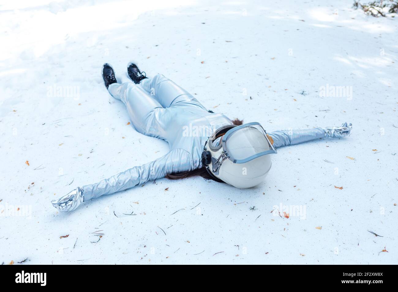 Full body fit calm spaceWoman in costume and helmet lying with arms outstretched on snowy glade in winter forest Stock Photo
