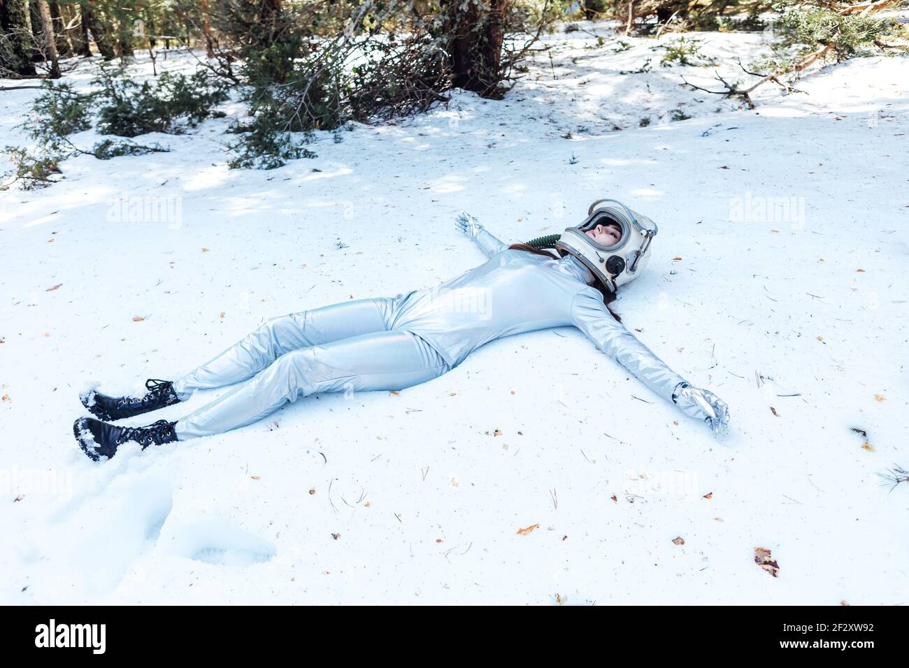 Full body fit calm spaceWoman in costume and helmet lying with arms outstretched on snowy glade in winter forest Stock Photo