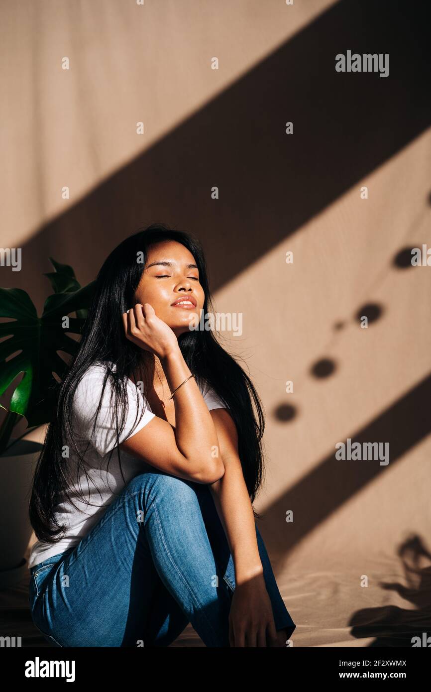 Attractive young Hispanic Woman wearing white cloth touching face with eyes closed in sun shadow Stock Photo