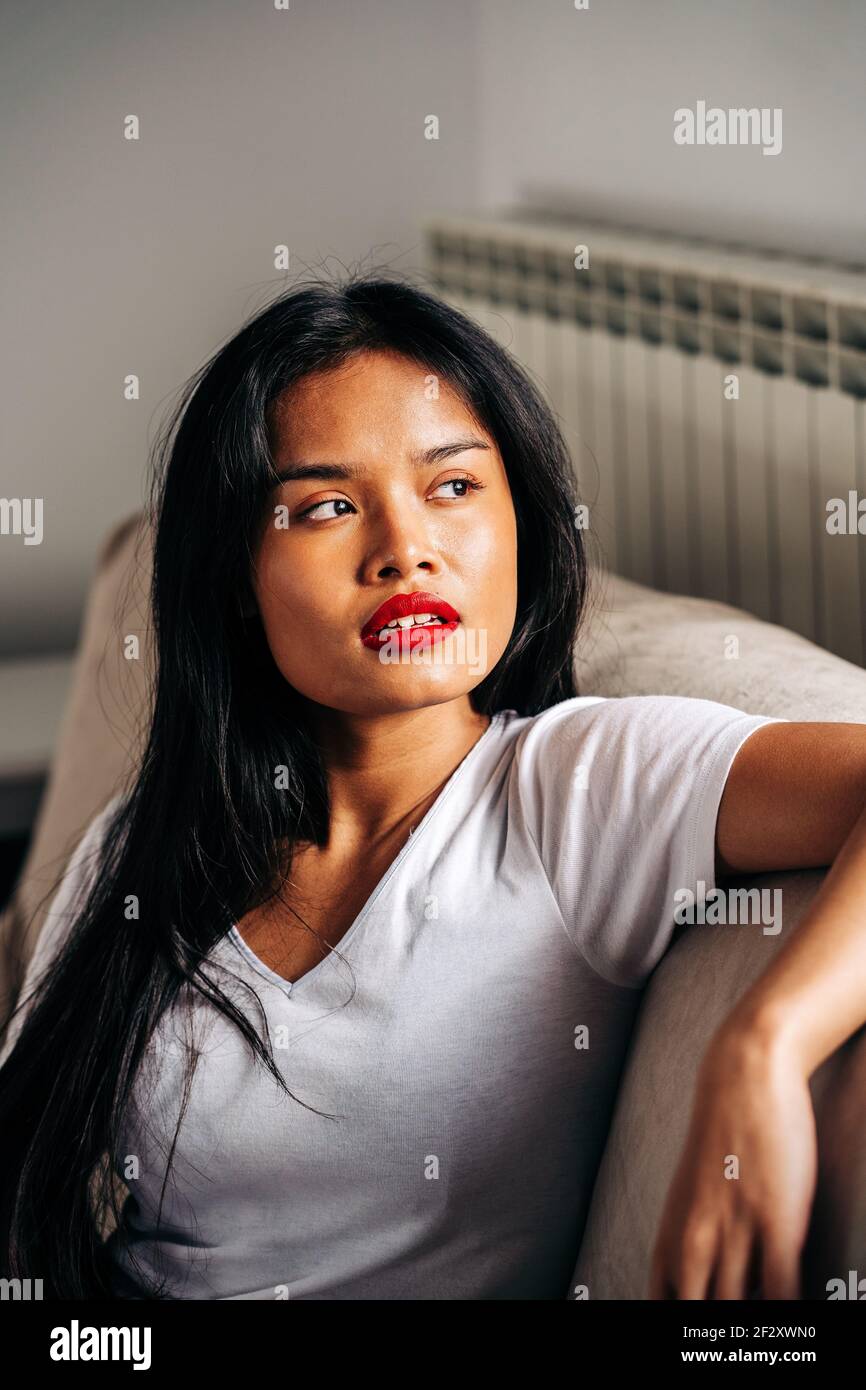 Portrait on serious ethnic female sitting on soft sofa looking away while having free time Stock Photo