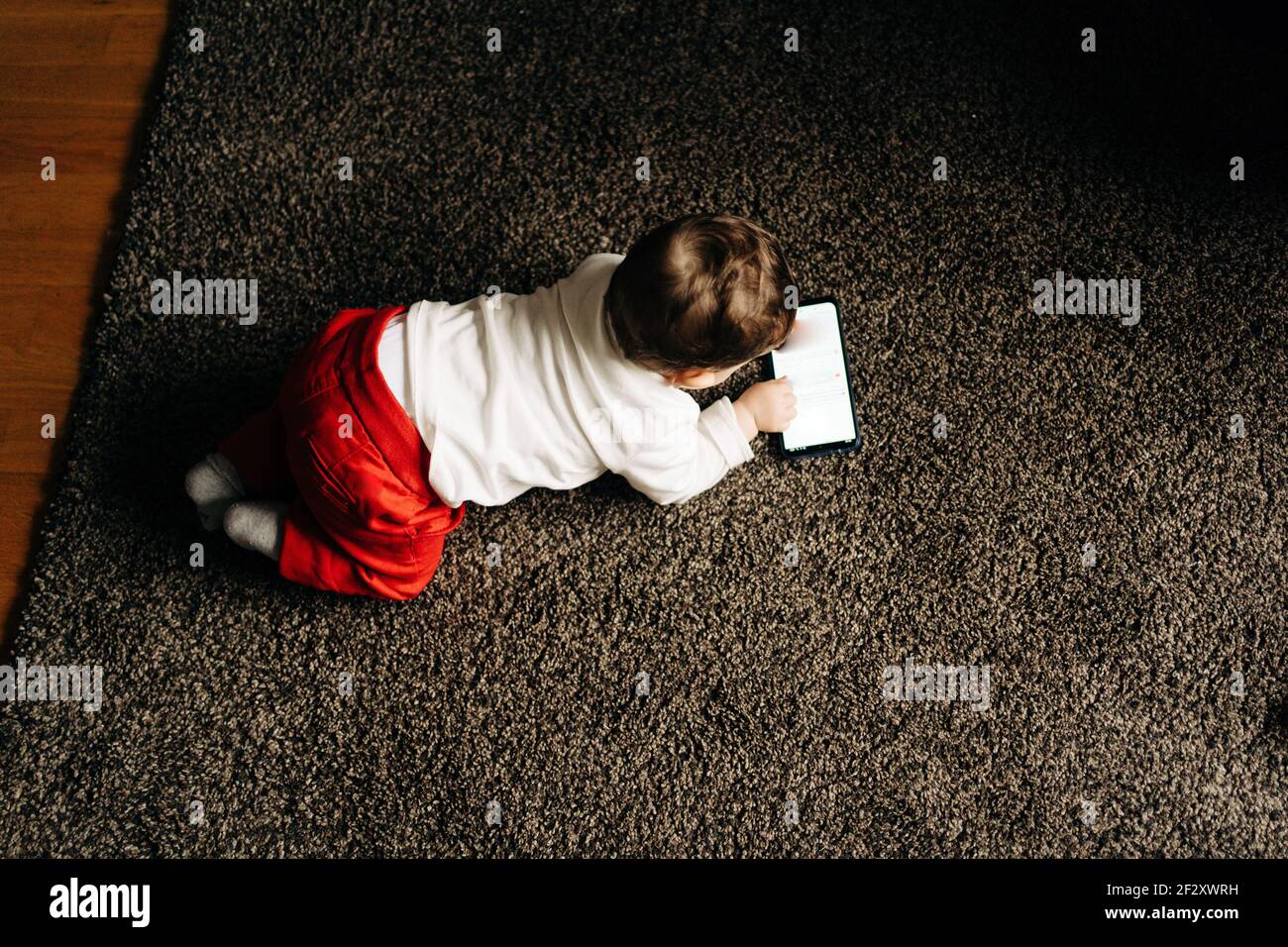 From above content little baby boy lying on fluffy carpet and watching funny  video on mobile phone in light living room Stock Photo - Alamy