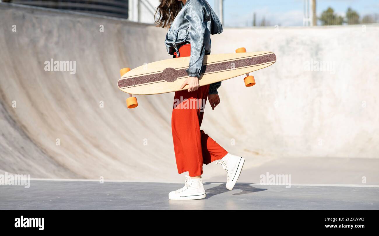 controller Feast good Side view of cropped unrecognizable happy young female in stylish apparel  walking with longboard on concrete skate park Stock Photo - Alamy