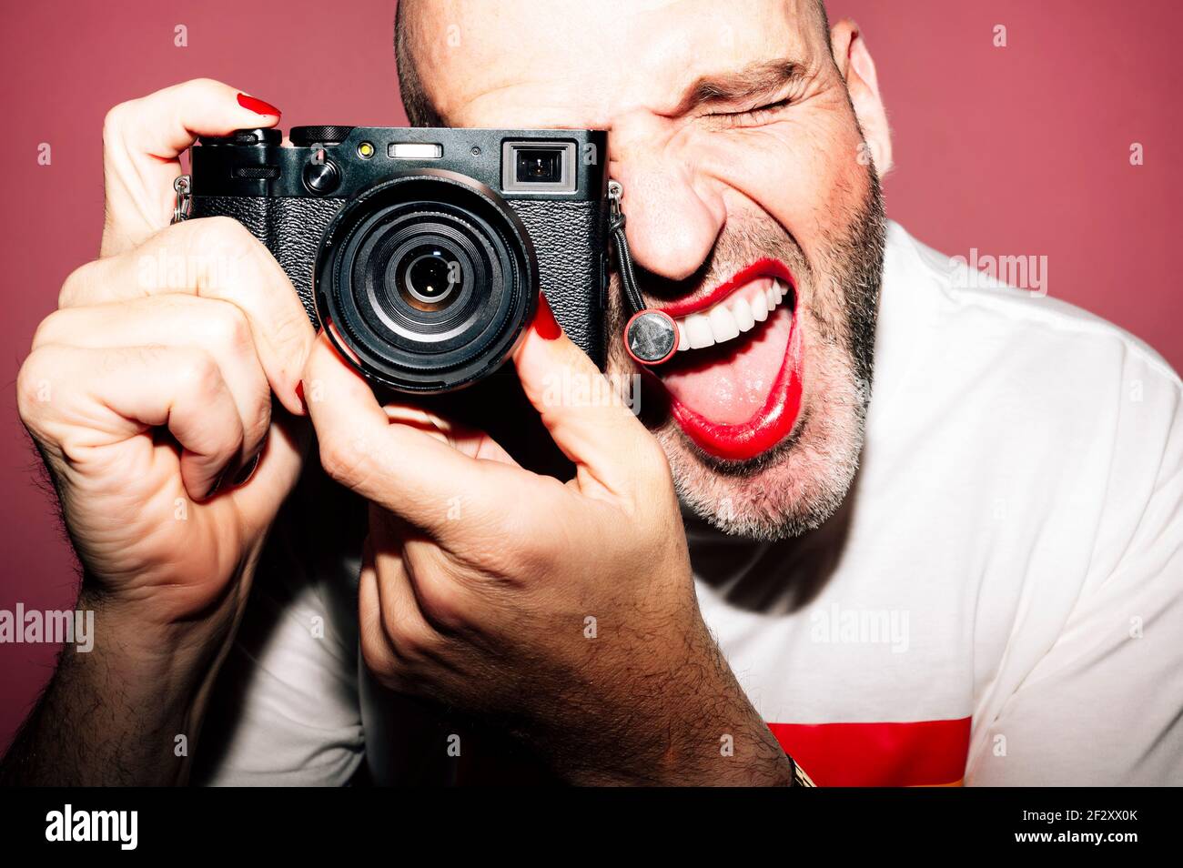 Crop bearded expressive homosexual male photographer in red lips and  manicure taking picture on vintage camera against pink background Stock  Photo - Alamy