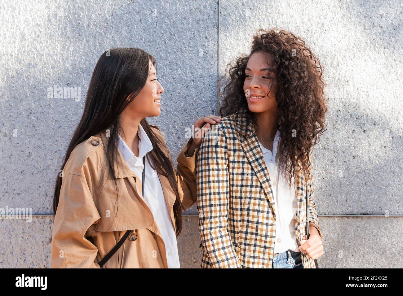 Young pensive women with long hair wearing trendy clothes standing on street and looking at each other Stock Photo
