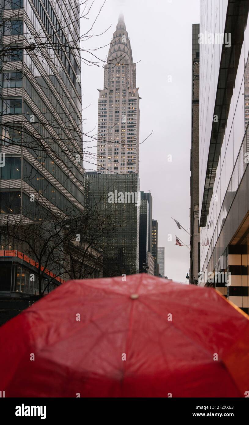 Wet red umbrella on urban New York street against famous Chrysler building on rainy gloomy autumn day Stock Photo