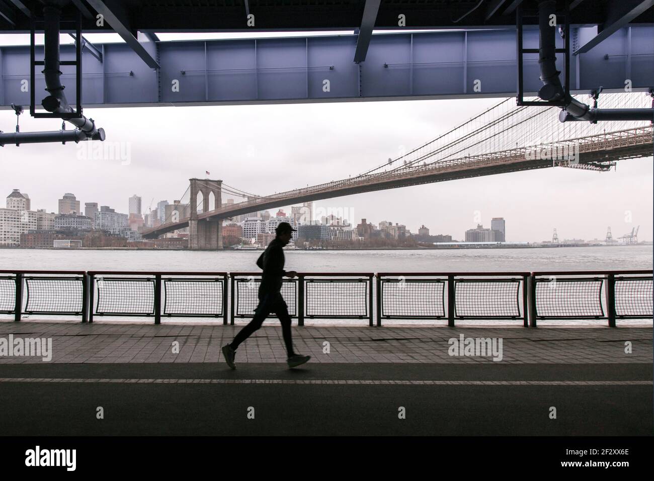 Side view anonymous sportsman jogging on paved embankment against urban city and suspension bridge on gloomy day Stock Photo