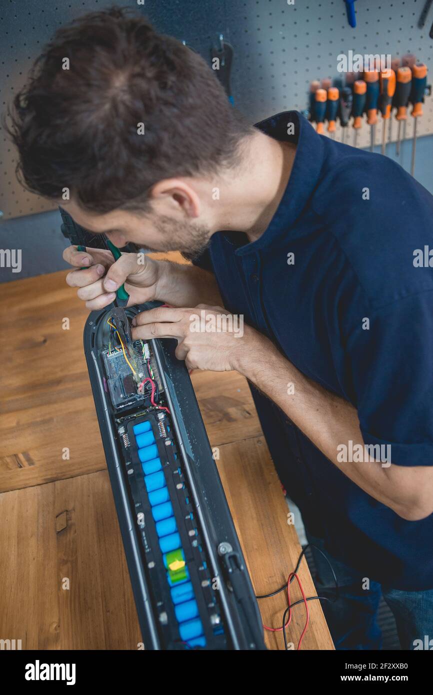 Side view of concentrated skilled male mechanic using multimeter while testing battery of electric scooter in workshop Stock Photo