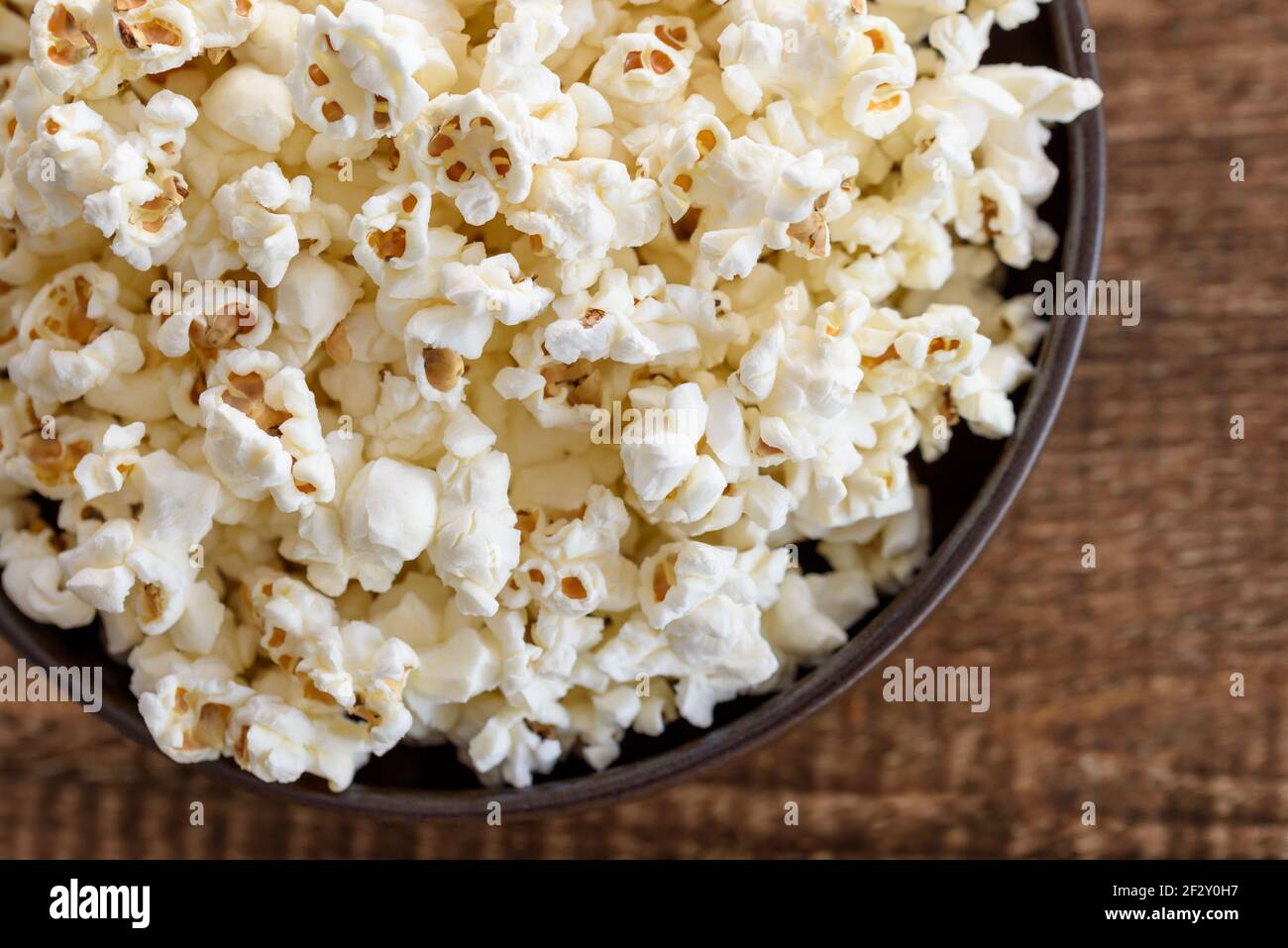 A bowl of popcorn, top-view, warm colors, light brown wooden background, flat lay, daylight macro close-up Stock Photo