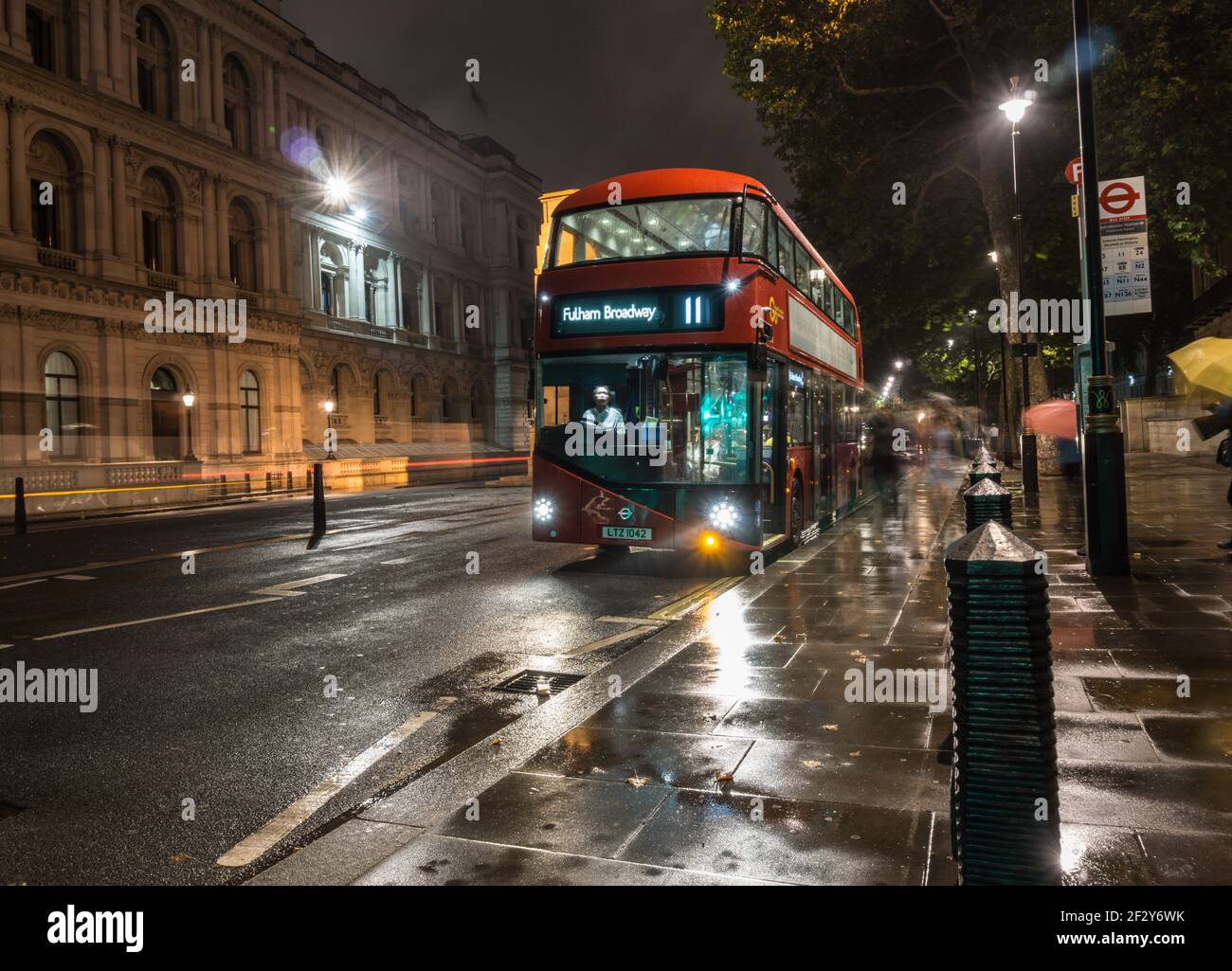 A red number 11 London bus for Fulham Broadway waiting at a bus stop in Whitehall on a rainy
