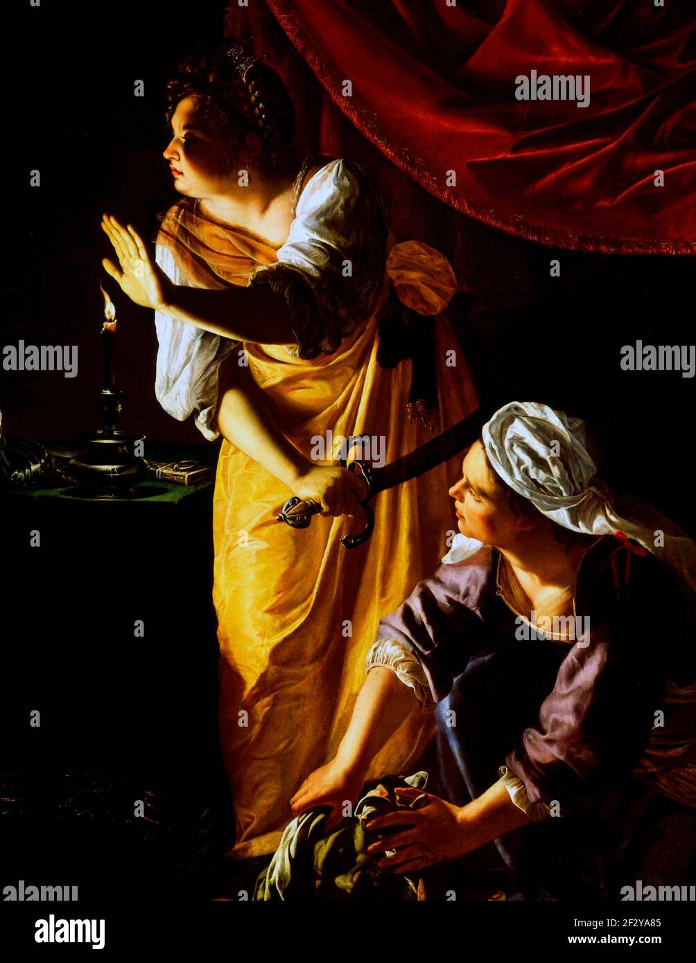 Judith and her Maidservant - Judith and her servant pause, seeming to hear a noise outside Holofernes’ tent. The shadowy interior is theatrically illuminated by a single candle. Judith’s hand shields her face from the glow, drawing attention to Holofernes’ discarded iron gauntlet. The viewer’s eye travels to the object in the maidservant’s hands: Holofernes’ severed head - Artemisia Gentileschi, circa 1625 Stock Photo