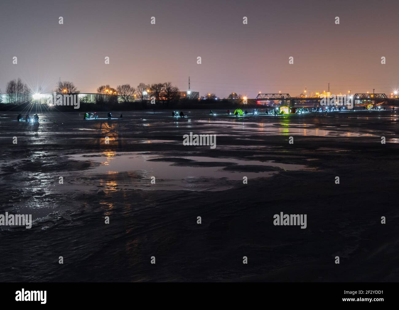 frozen river, night and ice anglers fish in the dark with artificial lights and everyone sits one after another in a strip in the middle of sleep Stock Photo