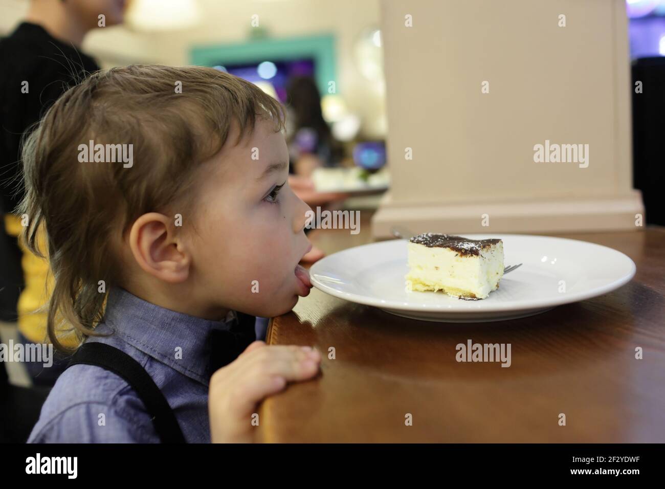 Kid licking plate with cake in the cafe Stock Photo