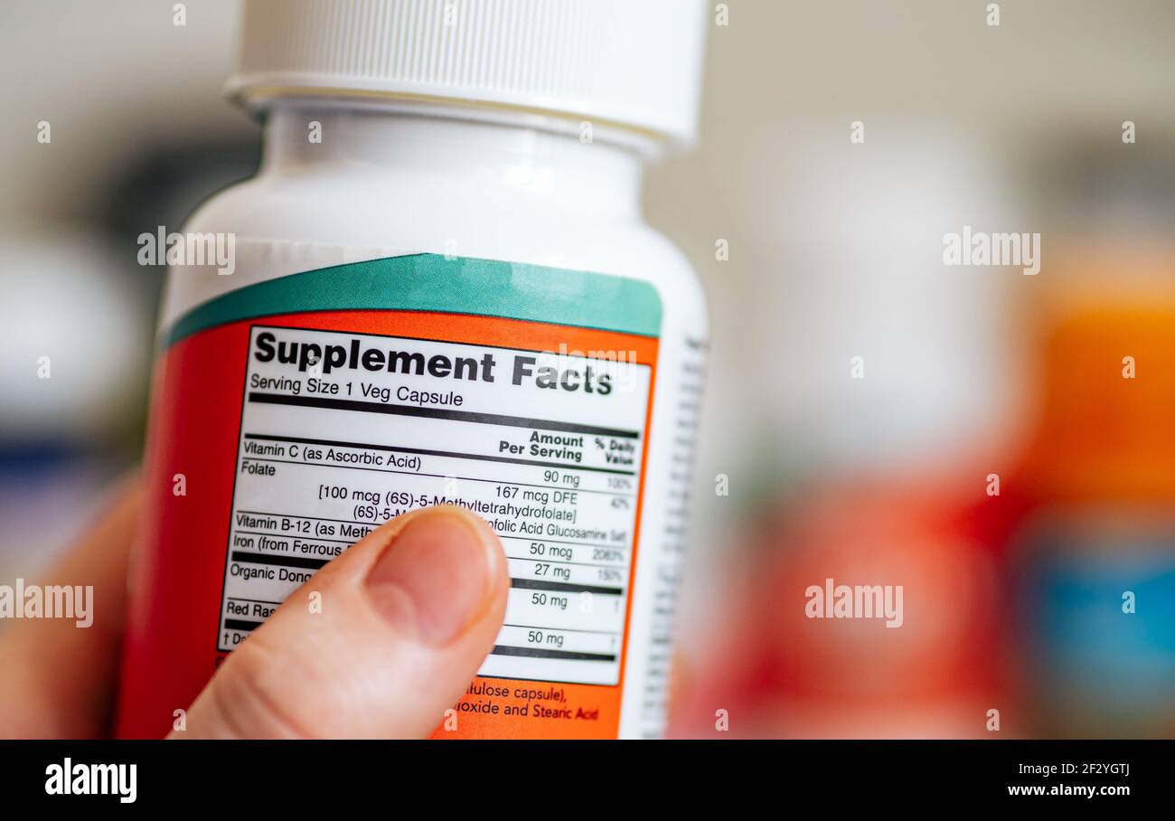 Supplement Facts concept. Close up view of jar with Supplement Facts information in female hand and defocused jars with different dietary supplement on blurred background. Copy space Stock Photo