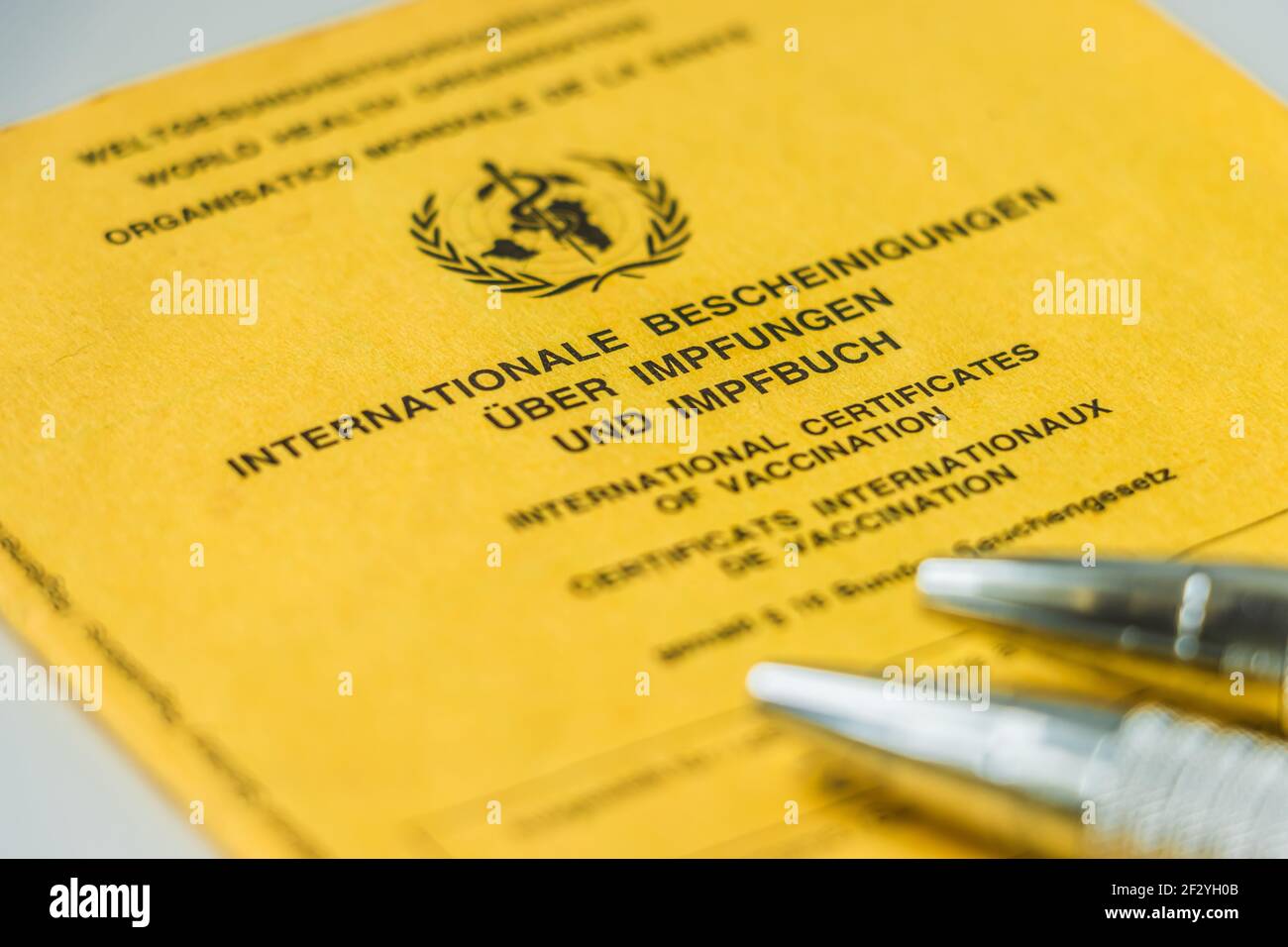 with two pens on yellow World Health Organization vaccination book. Cover sheet of the yellow vaccination certificate with proof of vaccinations. Stock Photo
