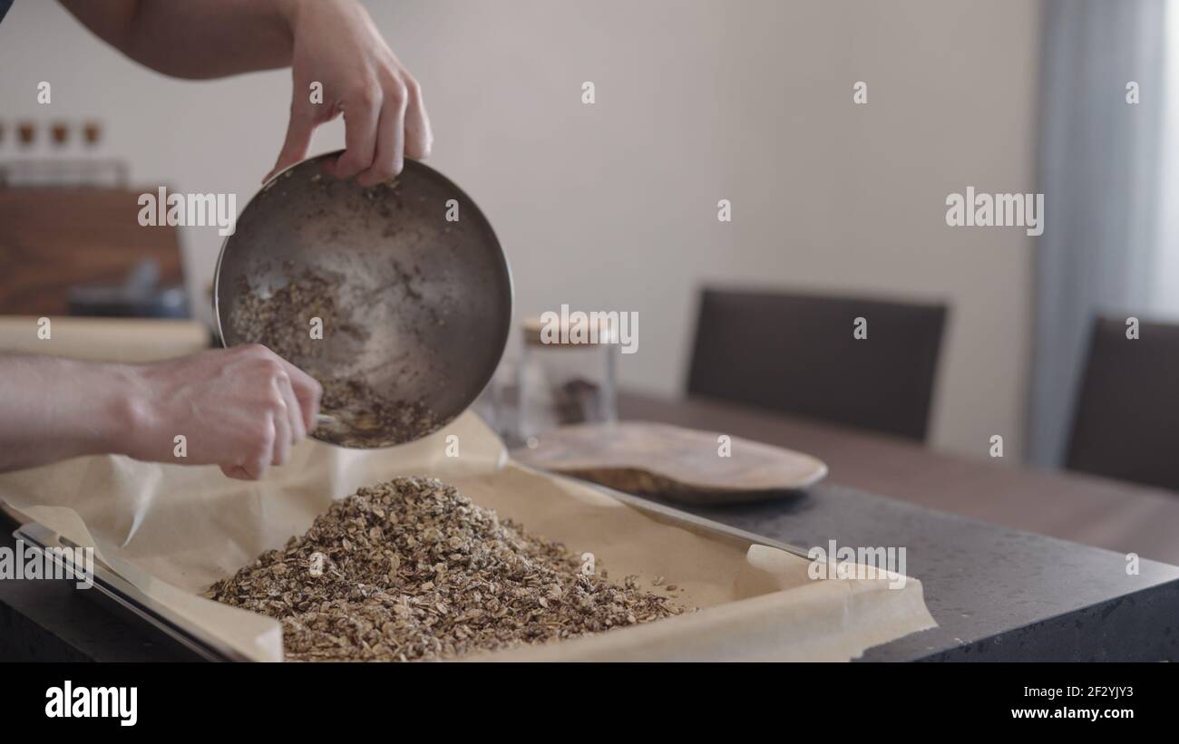man making granola pour it on baking tray with parchment paper, wide photo Stock Photo