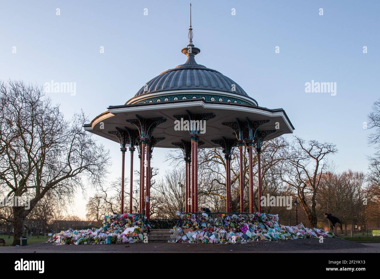 London, UK. 14th March, 2021. The flowers have been placed back neatly, and a few candles are still lit in memory of Sarah Everard and for women everywhere, following terrible scenes the night before where Police turned a peaceful vigil into an unsafe protest at Clapham Common Bandstand. Credit: Liam Asman/Alamy Live News Stock Photo
