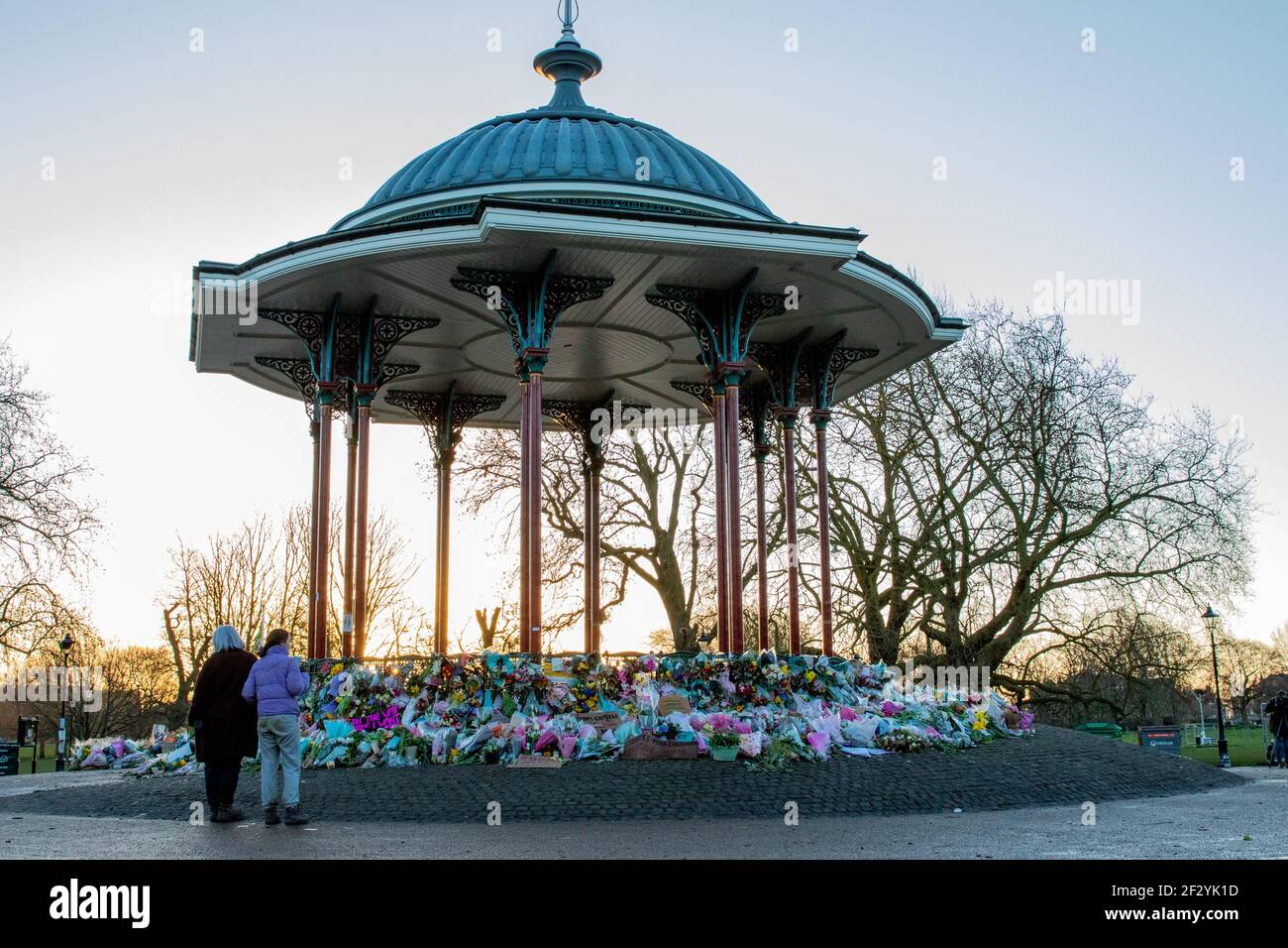 London, UK. 14th March, 2021. The flowers have been placed back neatly, and a few candles are still lit in memory of Sarah Everard and for women everywhere, following terrible scenes the night before where Police turned a peaceful vigil into an unsafe protest at Clapham Common Bandstand. Credit: Liam Asman/Alamy Live News Stock Photo