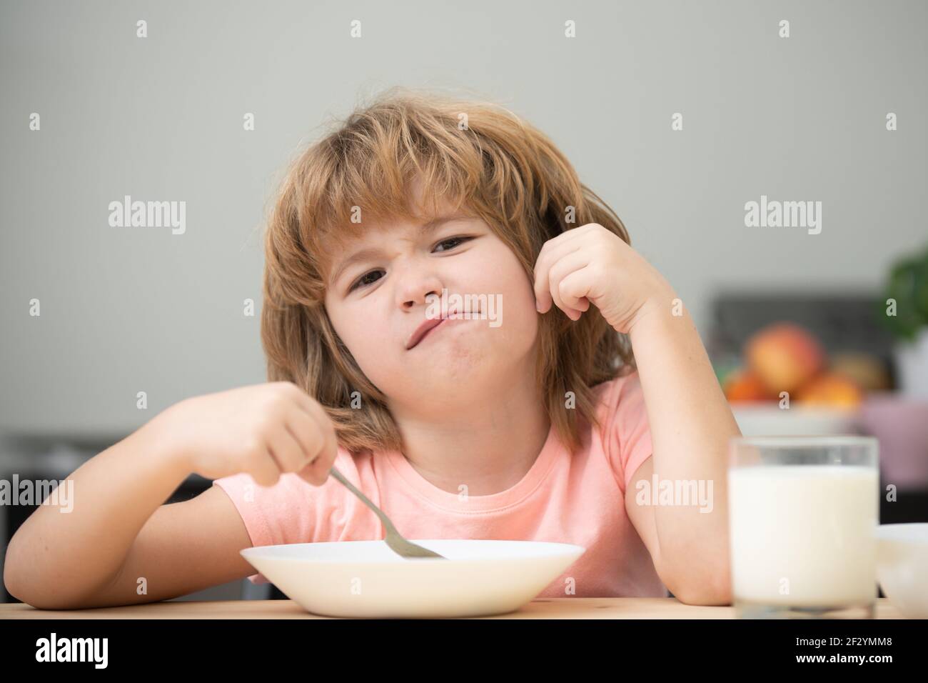 Child eating healthy food at home. Unhappy Caucasian child sit at table at home kitchen have no appetite. Upset little kid refuse to eat organic Stock Photo