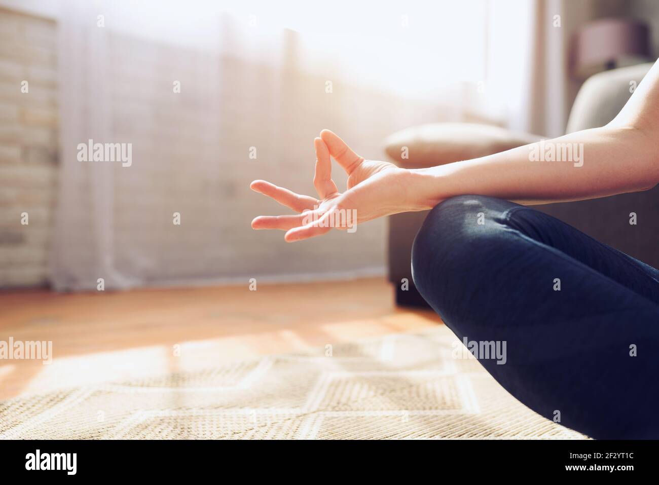 Young girl relaxing in yoga position at home in front of a bright window Stock Photo