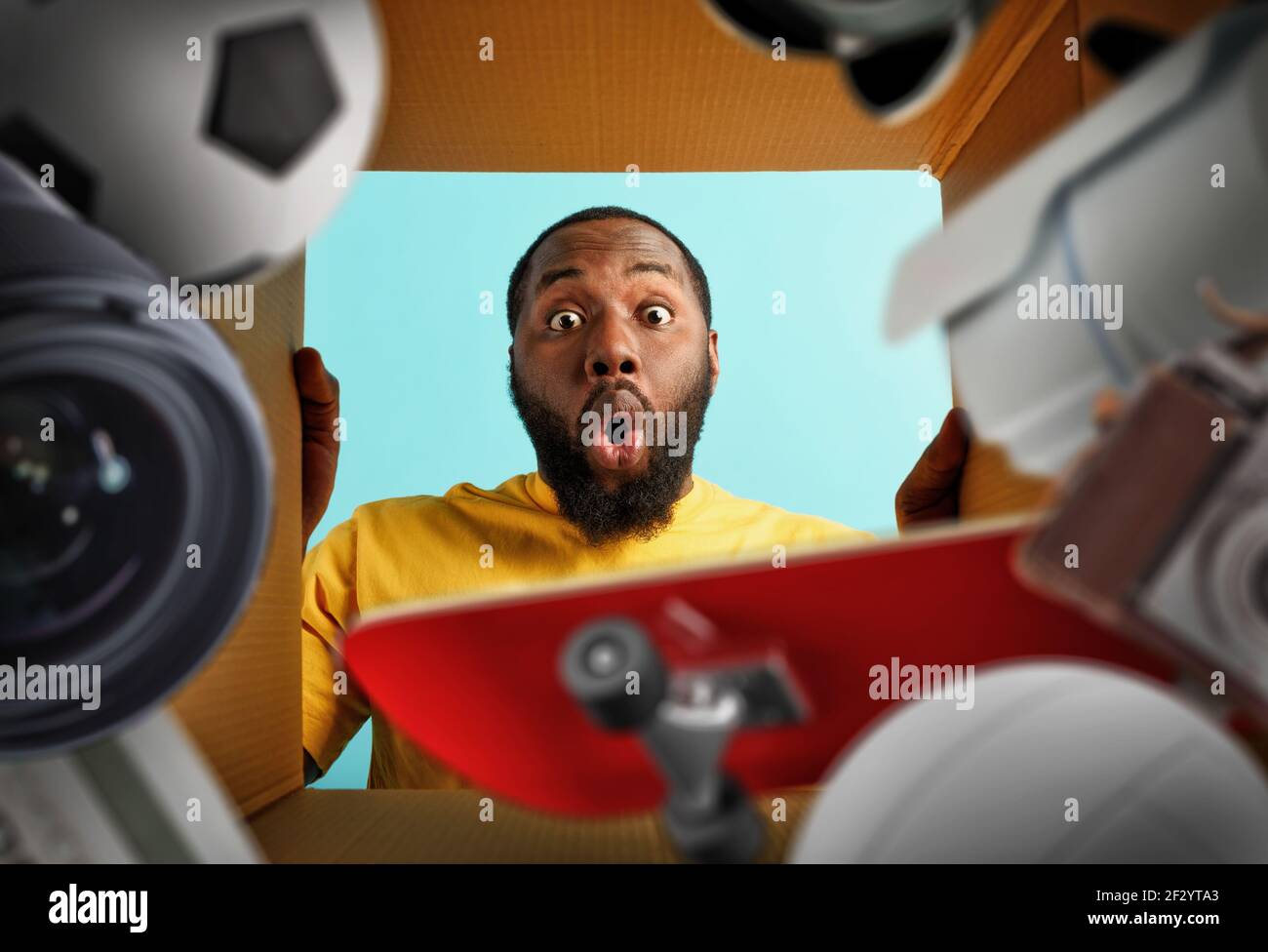 Happy man receives a package full of objects like camera lens, soccer ball, skateboard. happy and surprised expression. Stock Photo