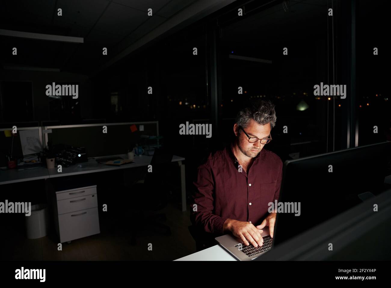 Portrait of a caucasian businessman working at his desk overtime in the dark office Stock Photo