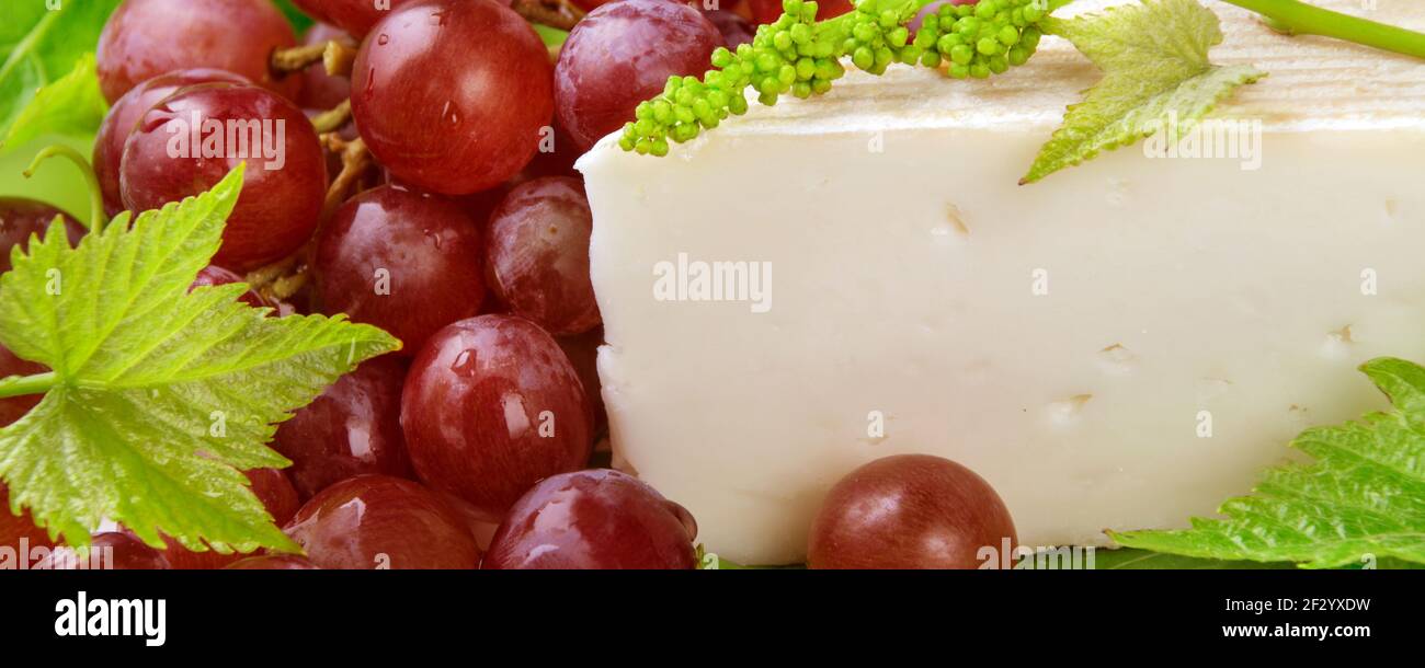 Käse mit roten Weintrauben und Weinblättern Banner Stock Photo