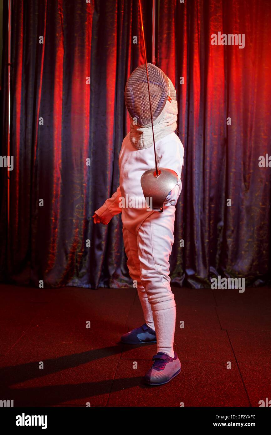 Girl in a fencing costume with a sword in hand, neon light. A young model trains and trains in movement, action. Sports, youth, healthy lifestyle. Stock Photo