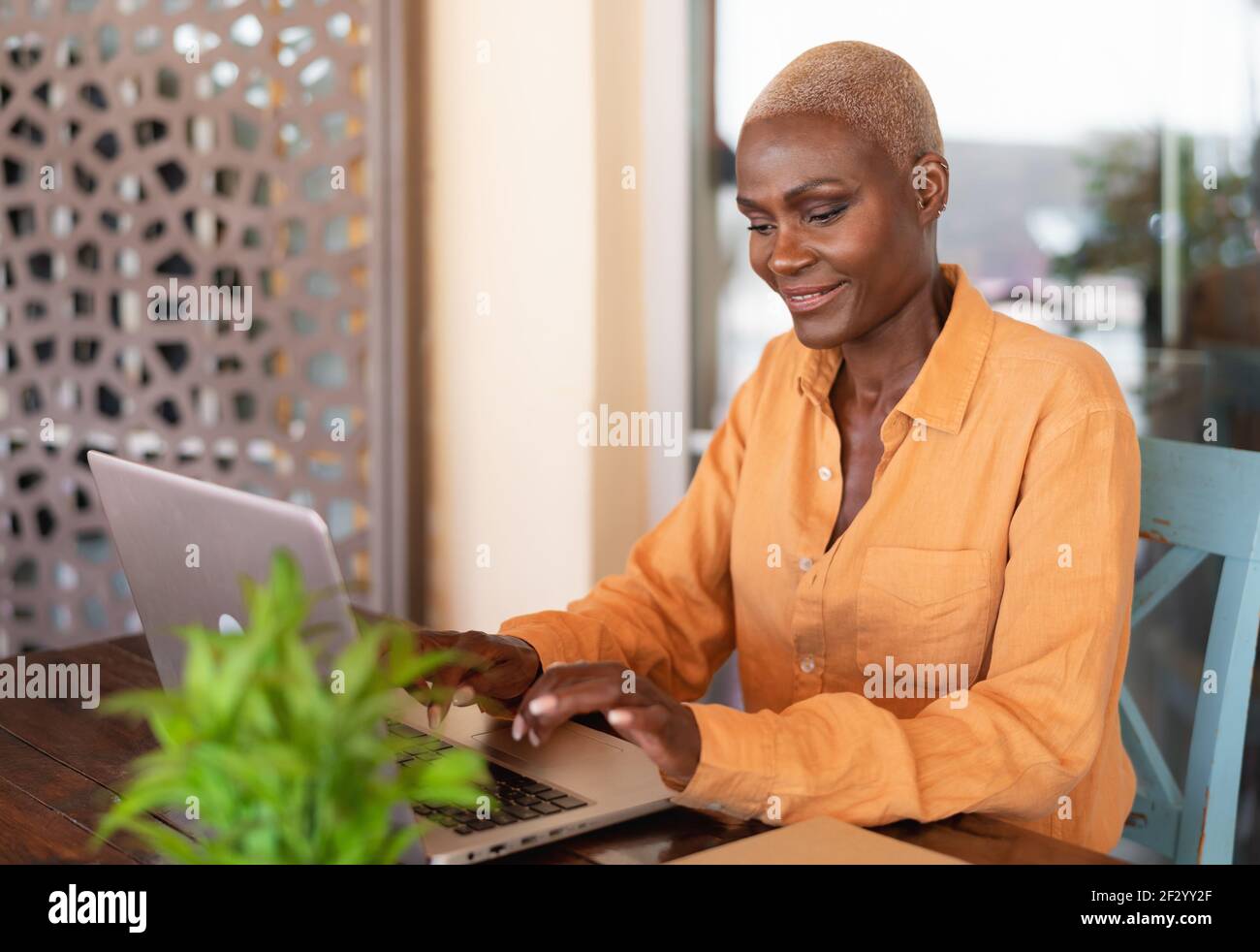 African woman working on laptop in bar restaurant - Afro female typing on computer - Digital nomad and freelance lifestyle concept Stock Photo