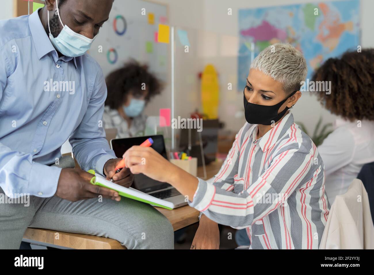 Young people in co-working creative space wearing surgical mask and keeping social distance to avoid corona virus spread Stock Photo