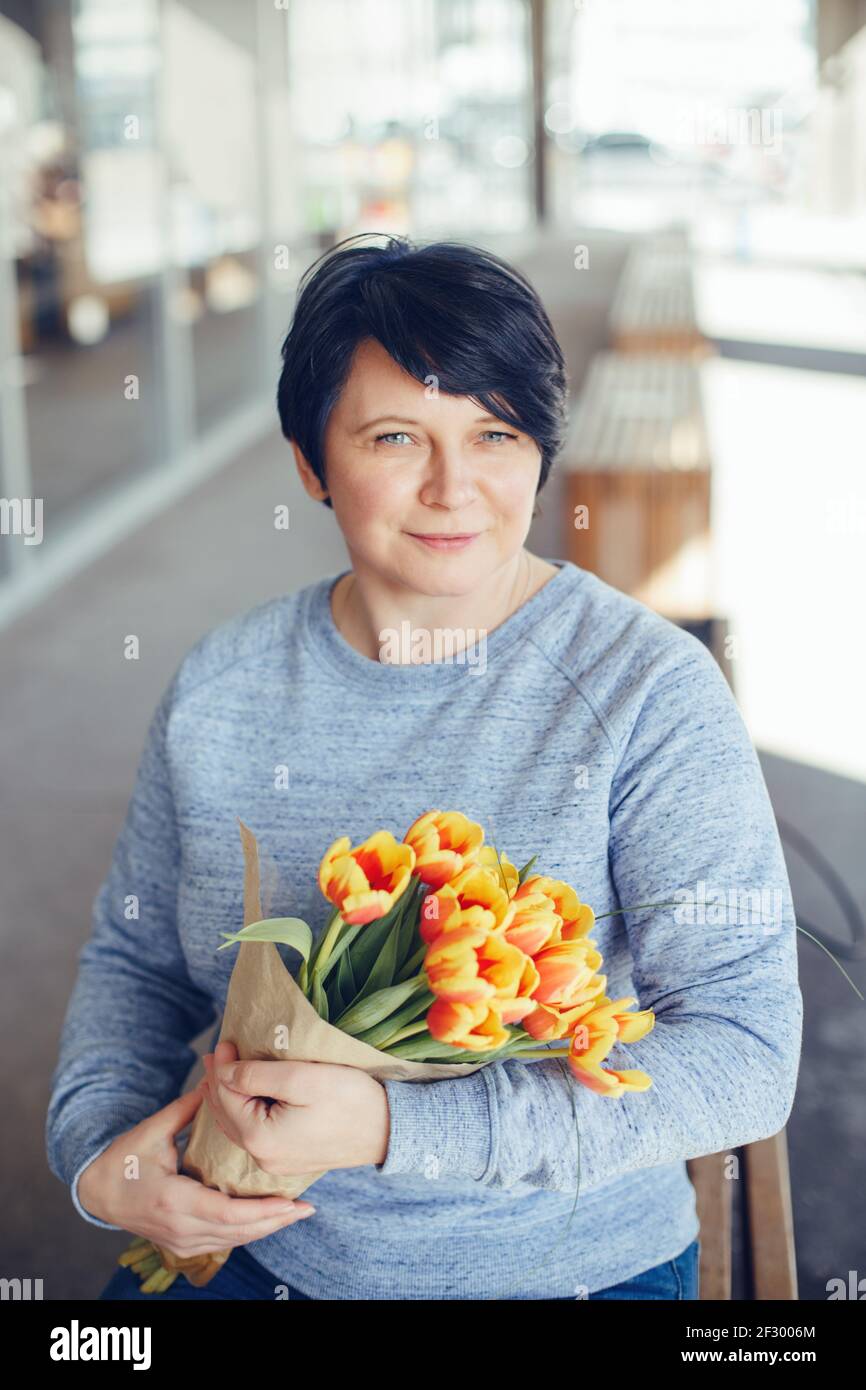 Adult middle age mature Caucasian woman with short black hair sitting on  bench outdoors and holding yellow red tulip flowers. Springtime and spring  Stock Photo - Alamy