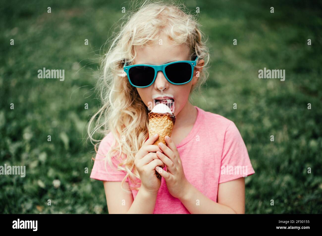 Cute funny adorable girl in sunglasses with dirty nose and moustaches eating ice cream from waffle cone. Happy cool child eating licking tasty sweet Stock Photo