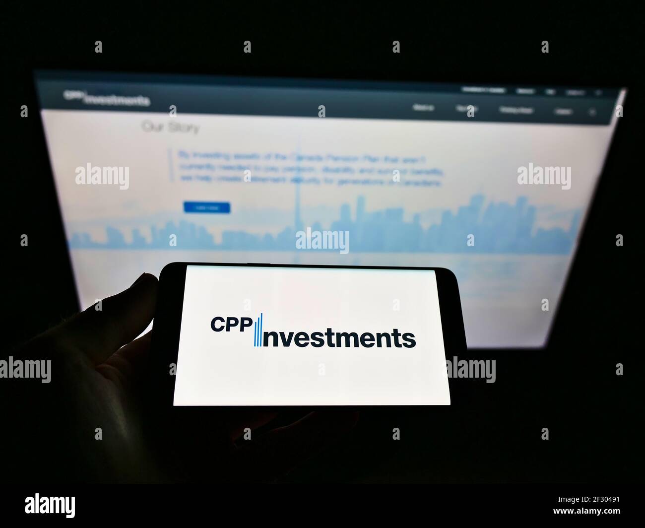 Person holding mobile phone with business logo of Canada Pension Plan Investment Board (CPPIB) on screen in front of webpage. Focus on phone display. Stock Photo
