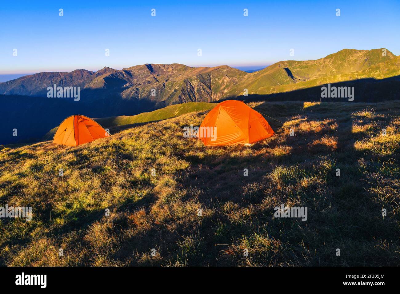 Campsite with colorful tents on the mountain ridge. Wild campgound in the mountains at sunrise, Fagaras mountains, Carpathians, Romania, Europe Stock Photo