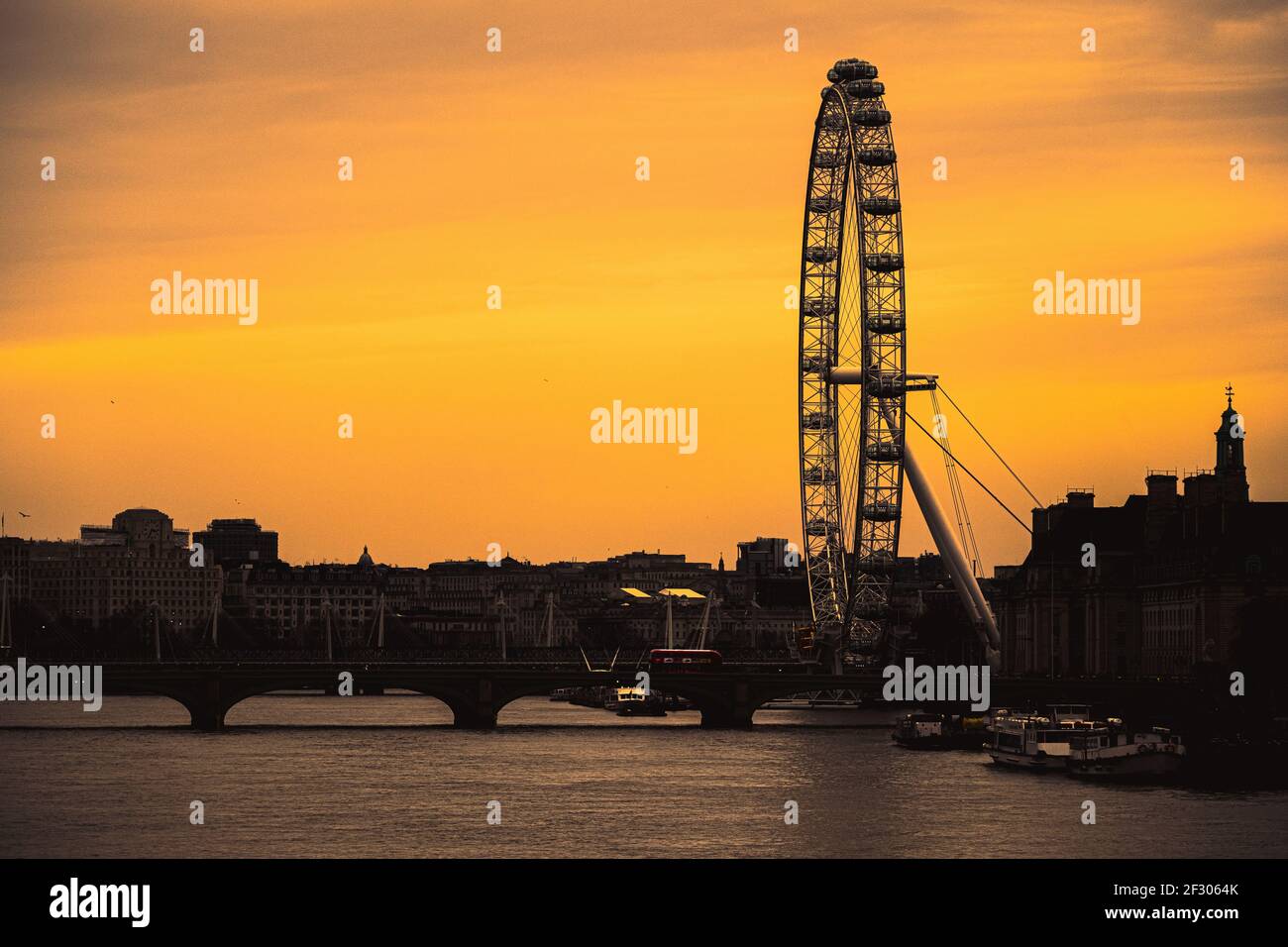 London UK February 2021 Amazing late sunset over London, silhouettes of the buildings and the London eye contrasting the dark orange sky. Red double d Stock Photo