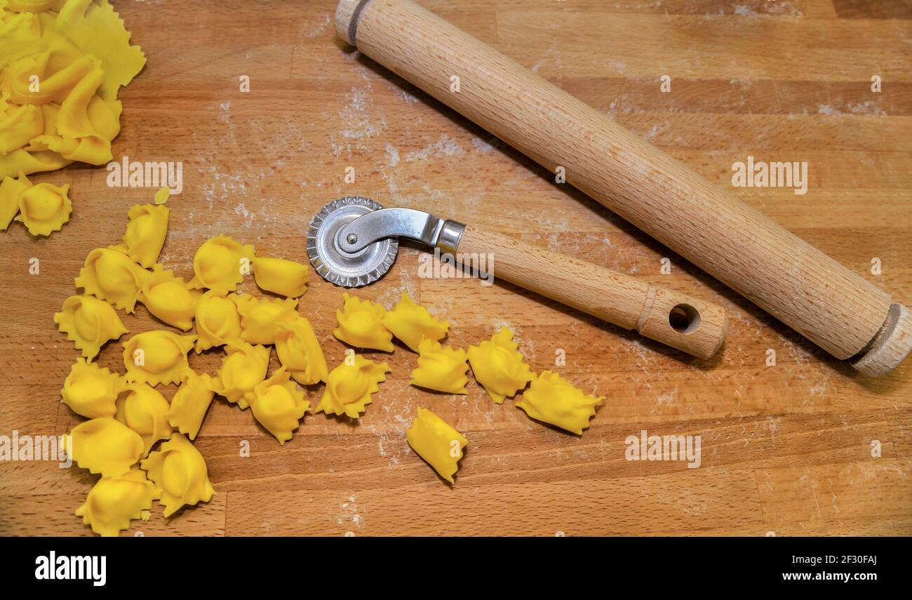 Ravioli del plin, typical pasta from Langhe, Piedmont, Italy - agnolotti with wheel knife and rolling pin on wooden cutting board Stock Photo
