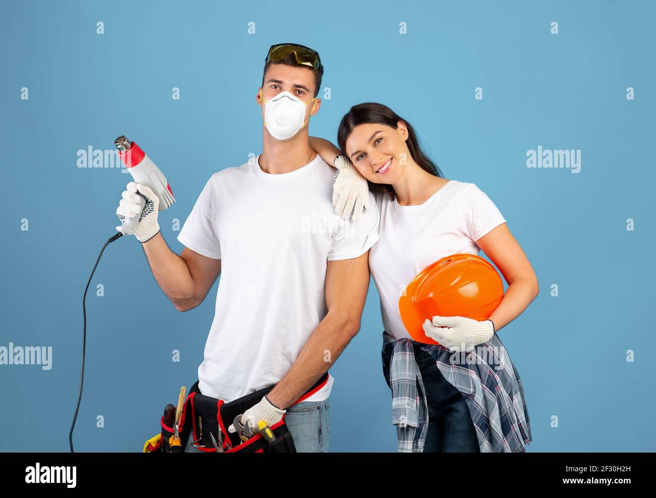 Young couple ready for repair, posing with construction tools over blue background Stock Photo
