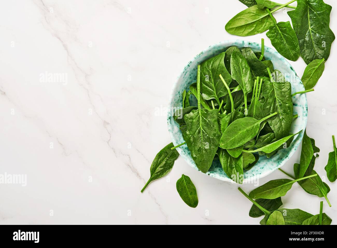 Fresh baby spinach leaves in ceramic beautiful bowl on light gray concrete background. Mock up. Top view. Stock Photo
