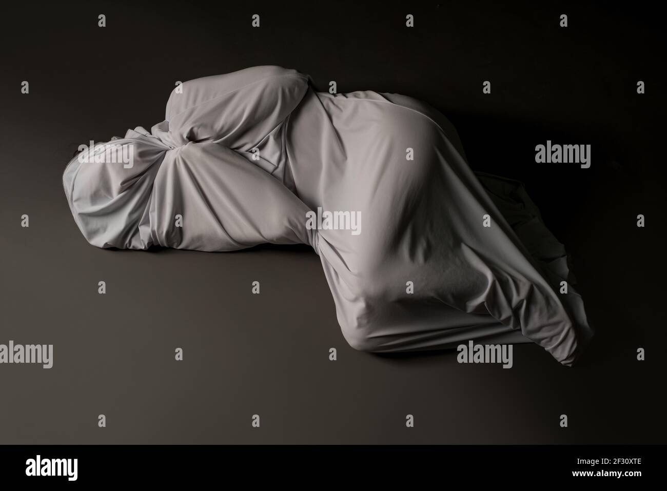 Anonymous person wrapped in cloth lying on floor Stock Photo