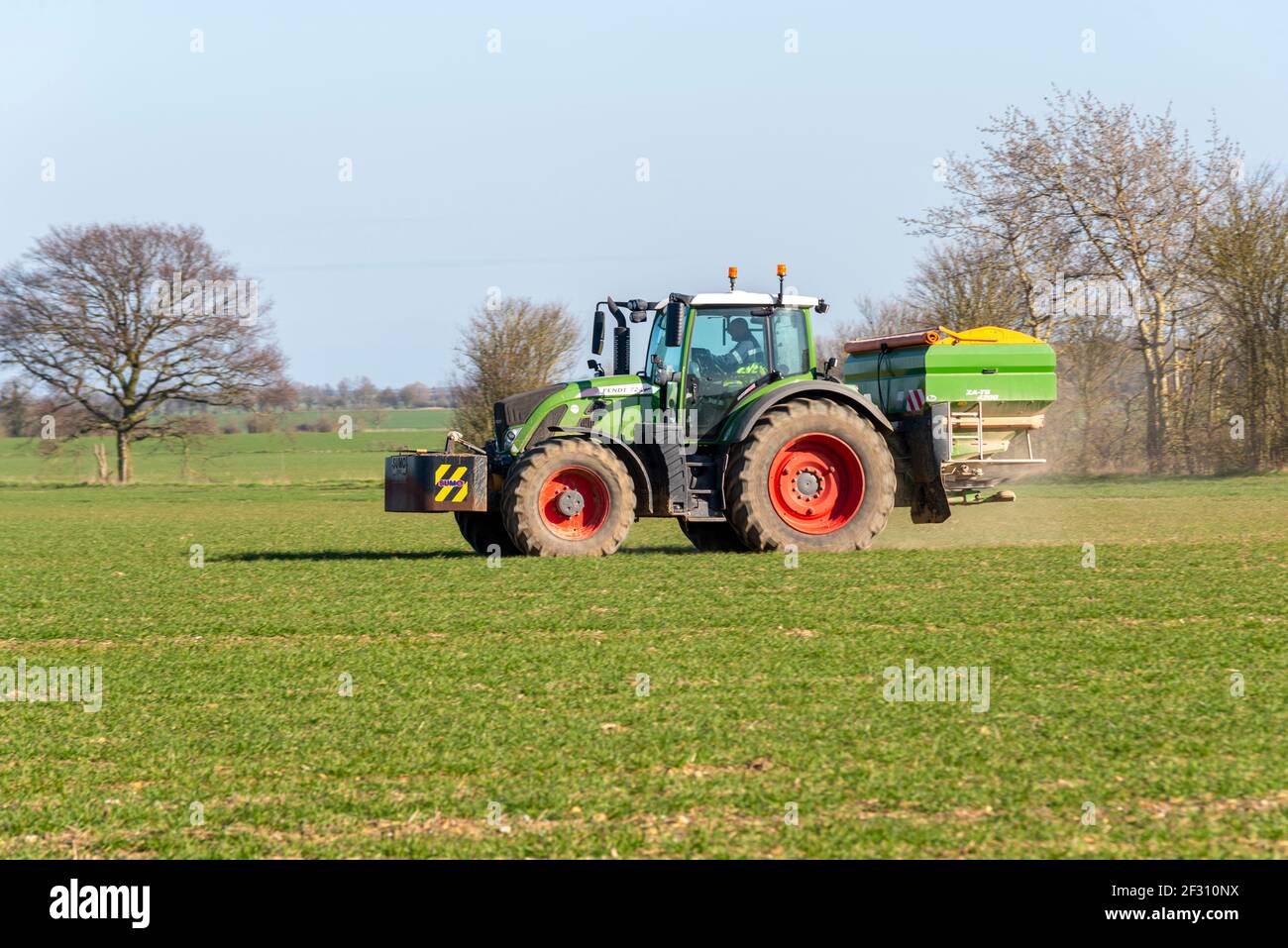 Tractor in Canewdon, Essex, UK. Fendt 724 Vario with ZA-TS 4200 litre mounted spreader. Spreading fertiliser on young crops in field. Agriculture Stock Photo