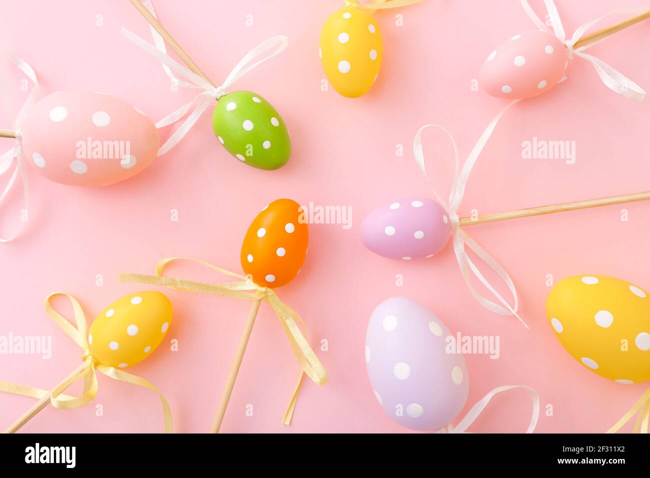 Colorful Easter eggs on sticks on pink background. Festive Easter holiday greeting card Stock Photo