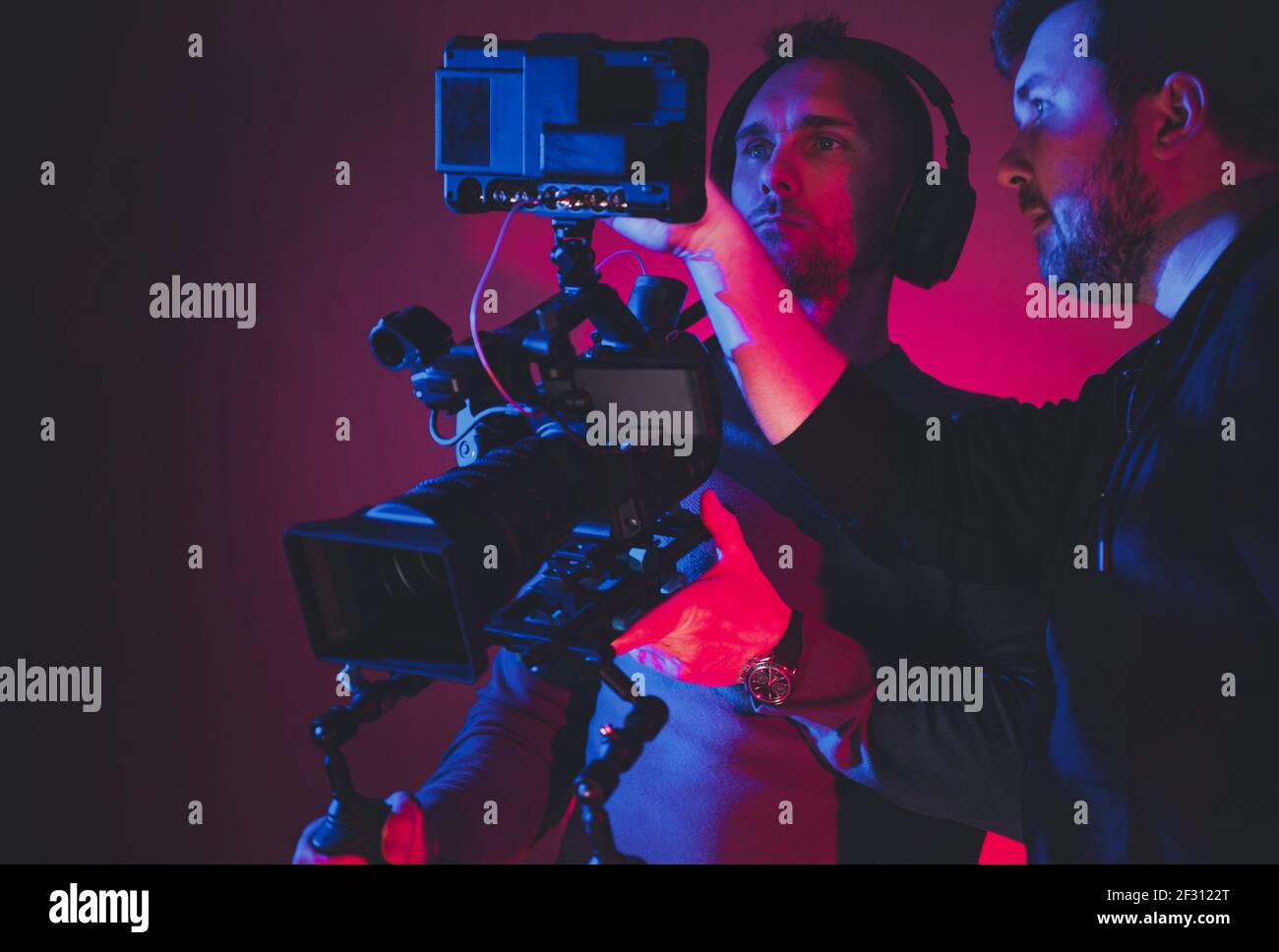Two Caucasian Men Film Camera Crew Consulting Newly Taken Footage Reviewing on Large Digital Storage Display. Digital Videography Industry Theme. Stock Photo