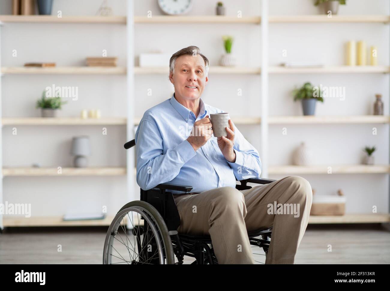 Positive senior impaired man in wheelchair drinking coffee or tea at home Stock Photo