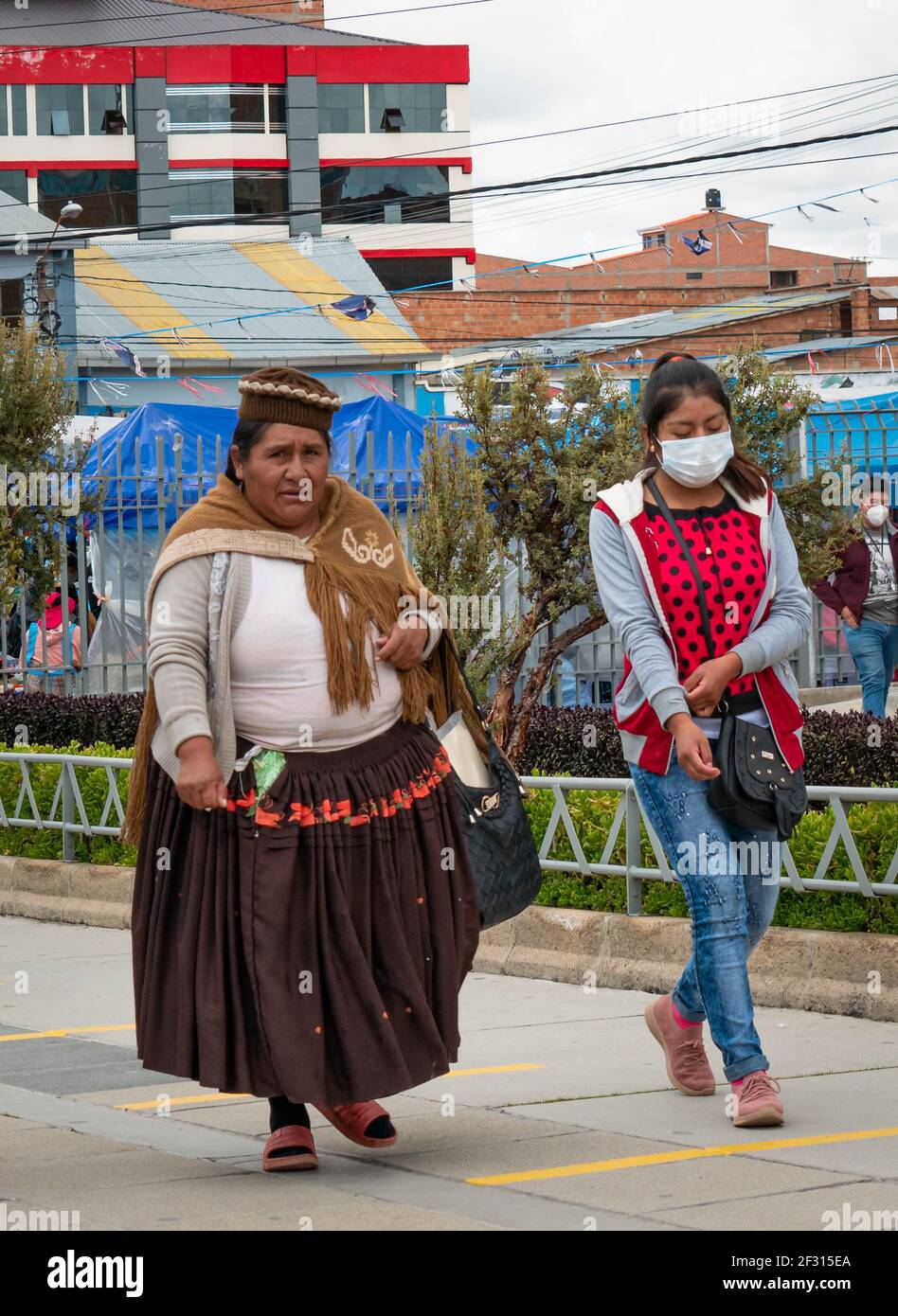 El Alto, La Paz, Bolivia - February 11 2021: Bolivian Indigenous Woman Known as 'Cholita', is Walking with a Young Woman Wearing a Mask Stock Photo