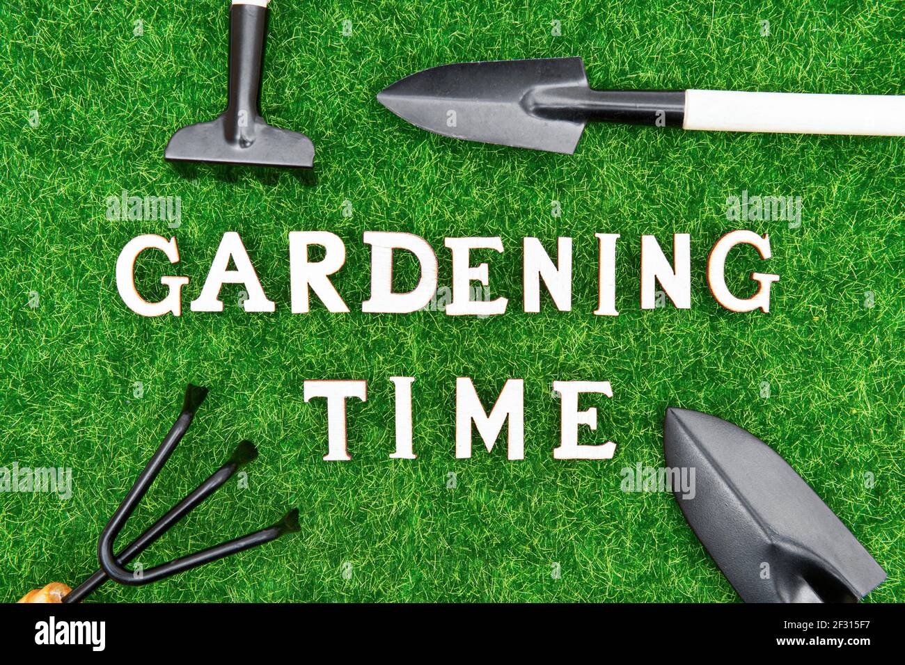 Crop view of various hand tools on synthetic grass with text made of wooden letters. Gardening time concept. Stock Photo