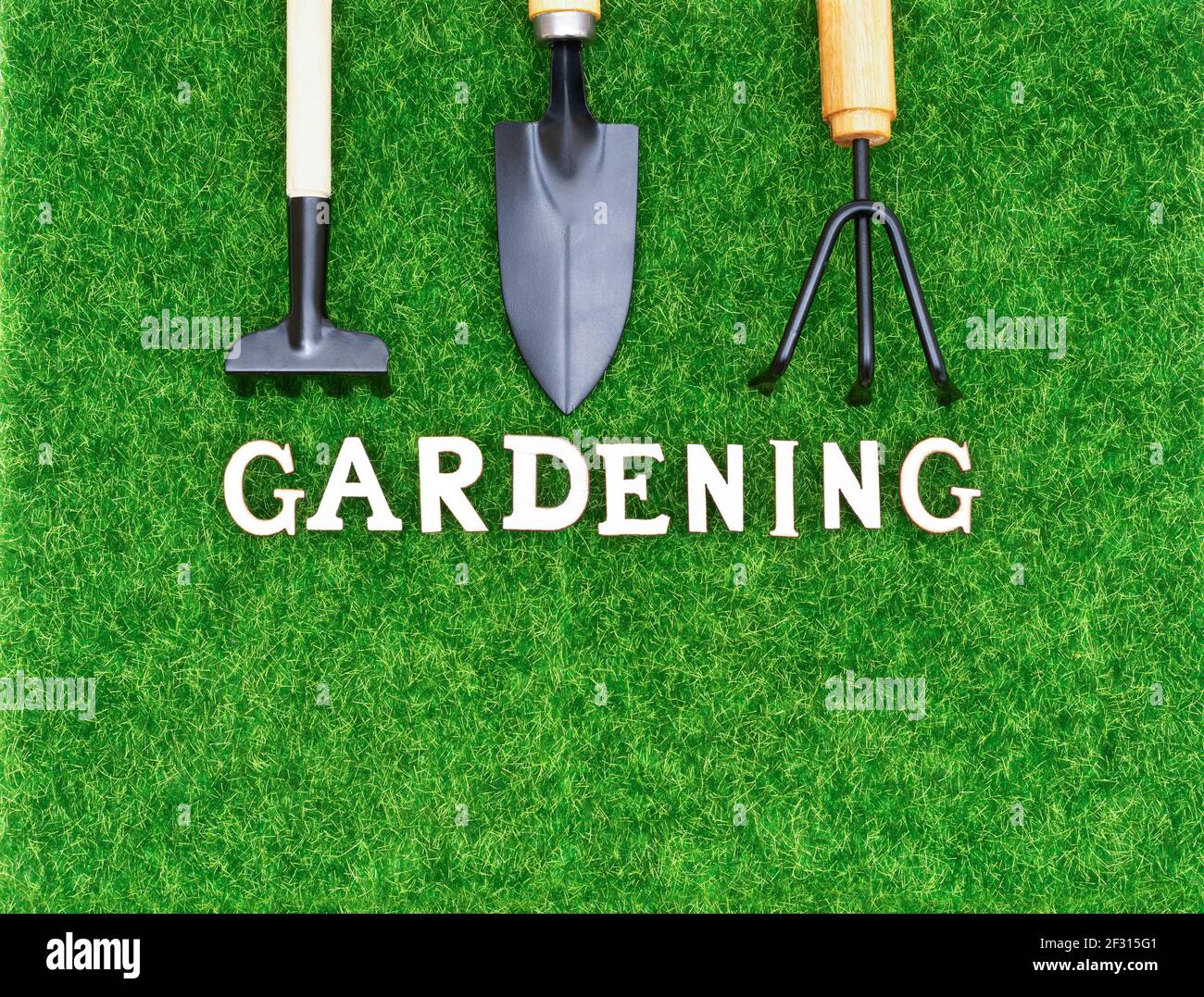 Garden hand tools on synthetic grass with lettering GARDENING made of wooden letters. Stock Photo