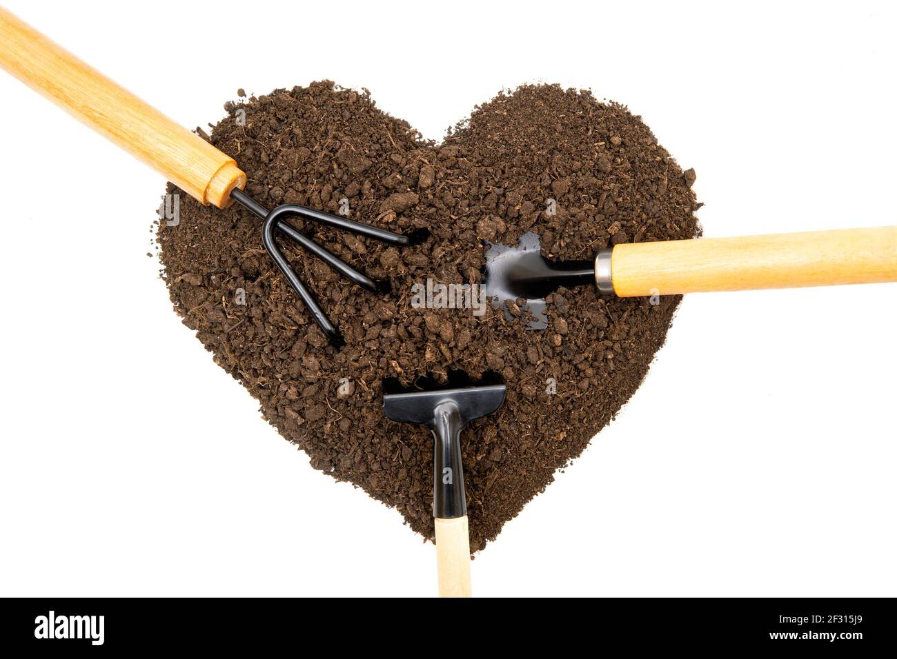 Various garden hand tools in a heart-shaped pile of soil isolated on white background. Gardening obsession concept. Stock Photo